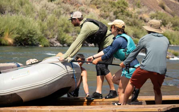 a group of outward bound students use a rope to launch a raft into a river